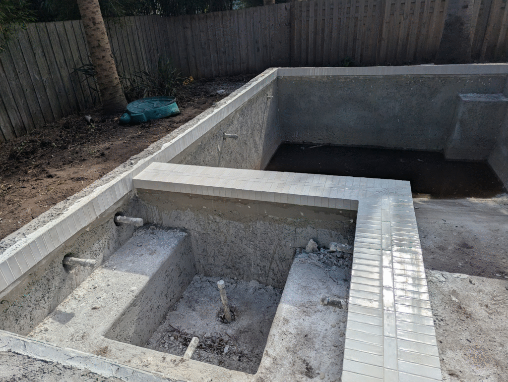 Installation of vertical waterline tile on spa wall using rectangular glass tile during pool construction