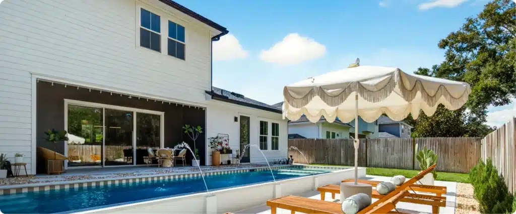 Backyard view of modern coastal home with pool, loungers, and scalloped umbrella creating a relaxed retreat
