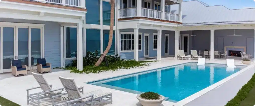 Poolside view of coastal home with covered outdoor living space, fireplace, and oceanfront pool