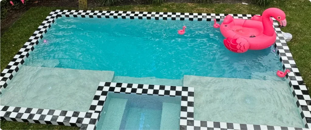 Side view of retro modern pool featuring black-and-white checkerboard tile, raised deck-level spa, and playful flamingo floats